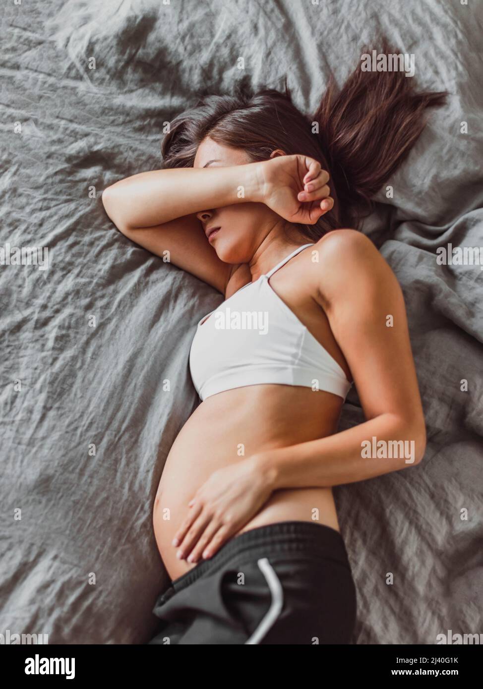 Tired pregnant woman sleeping on bed hiding face crying in depression or feeling morning sickness nausea. Mental health, fatigue, stress during Stock Photo