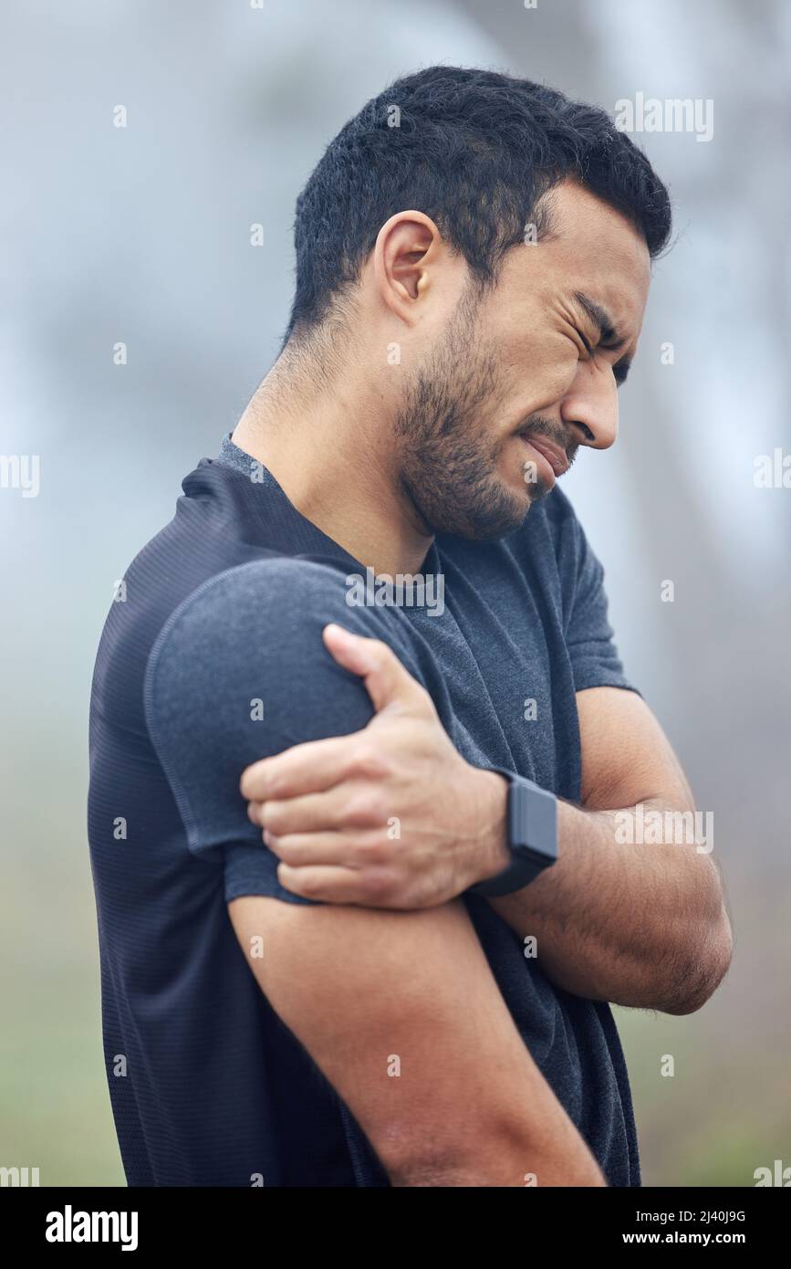 This pain is becoming more unbearable by the minute. Shot of a sporty young man holding his shoulder in pain while exercising outdoors. Stock Photo