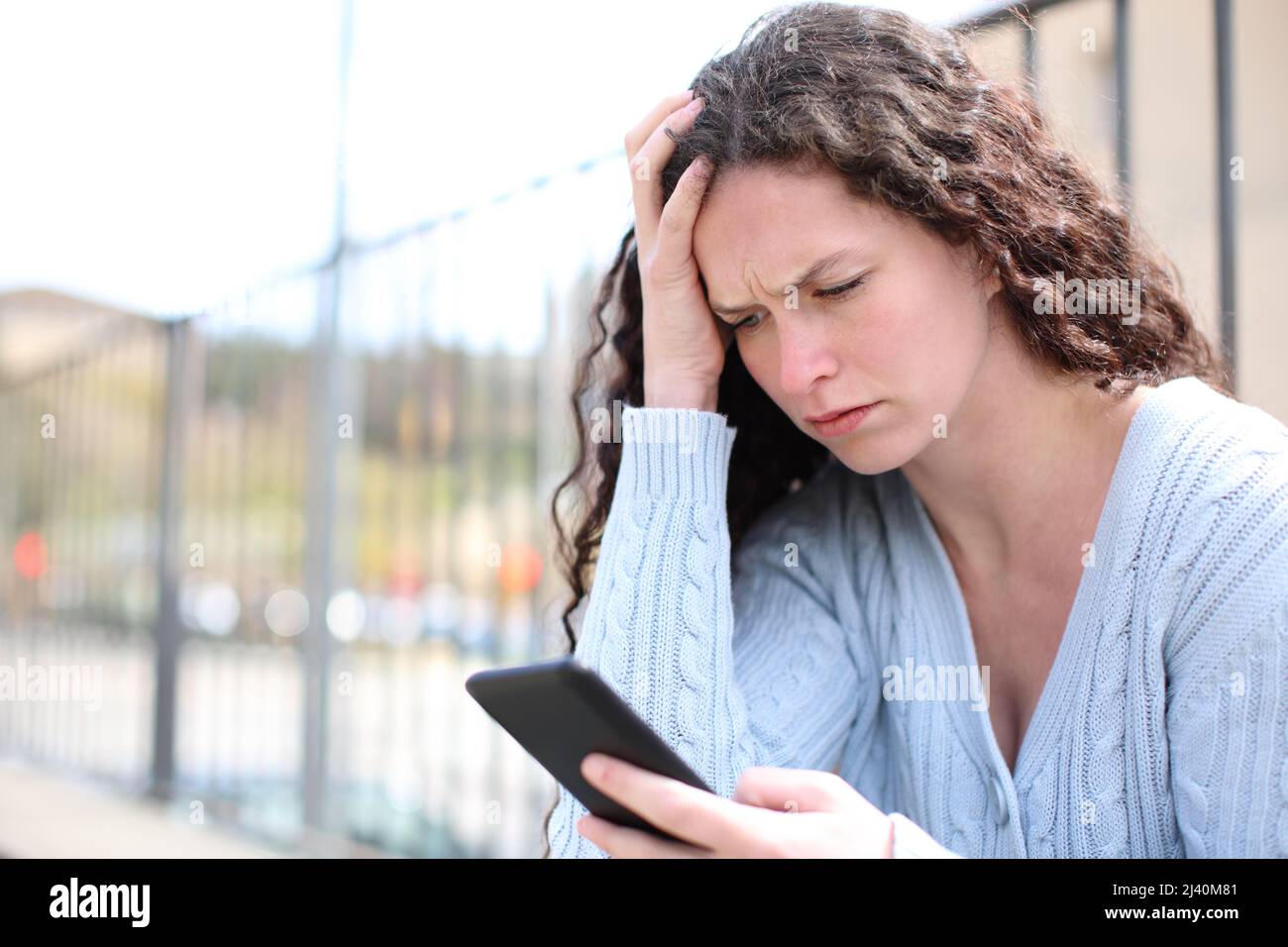 Worried woman checking cell phone sitting in the street Stock Photo