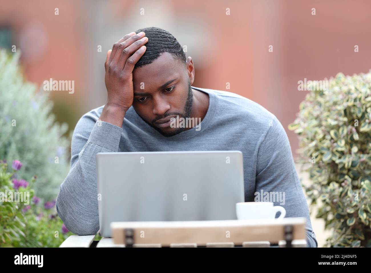 Front view portrait of a concerned man with black skin using laptop in a bar terrace Stock Photo