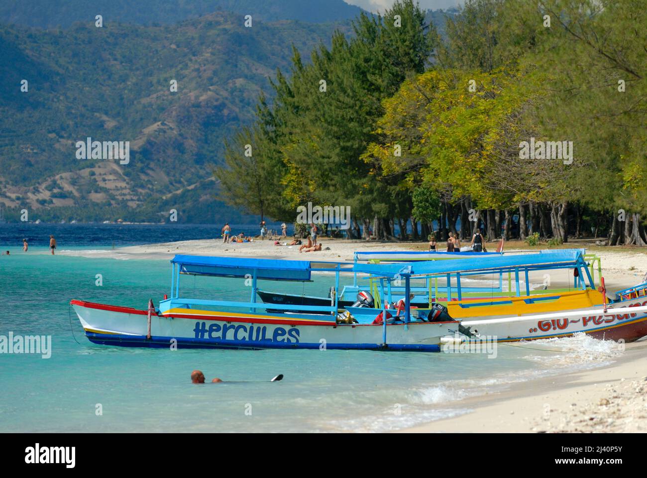 Tourists swim and relax and boats moored on one of Gili Trawangan's beaches. Stock Photo