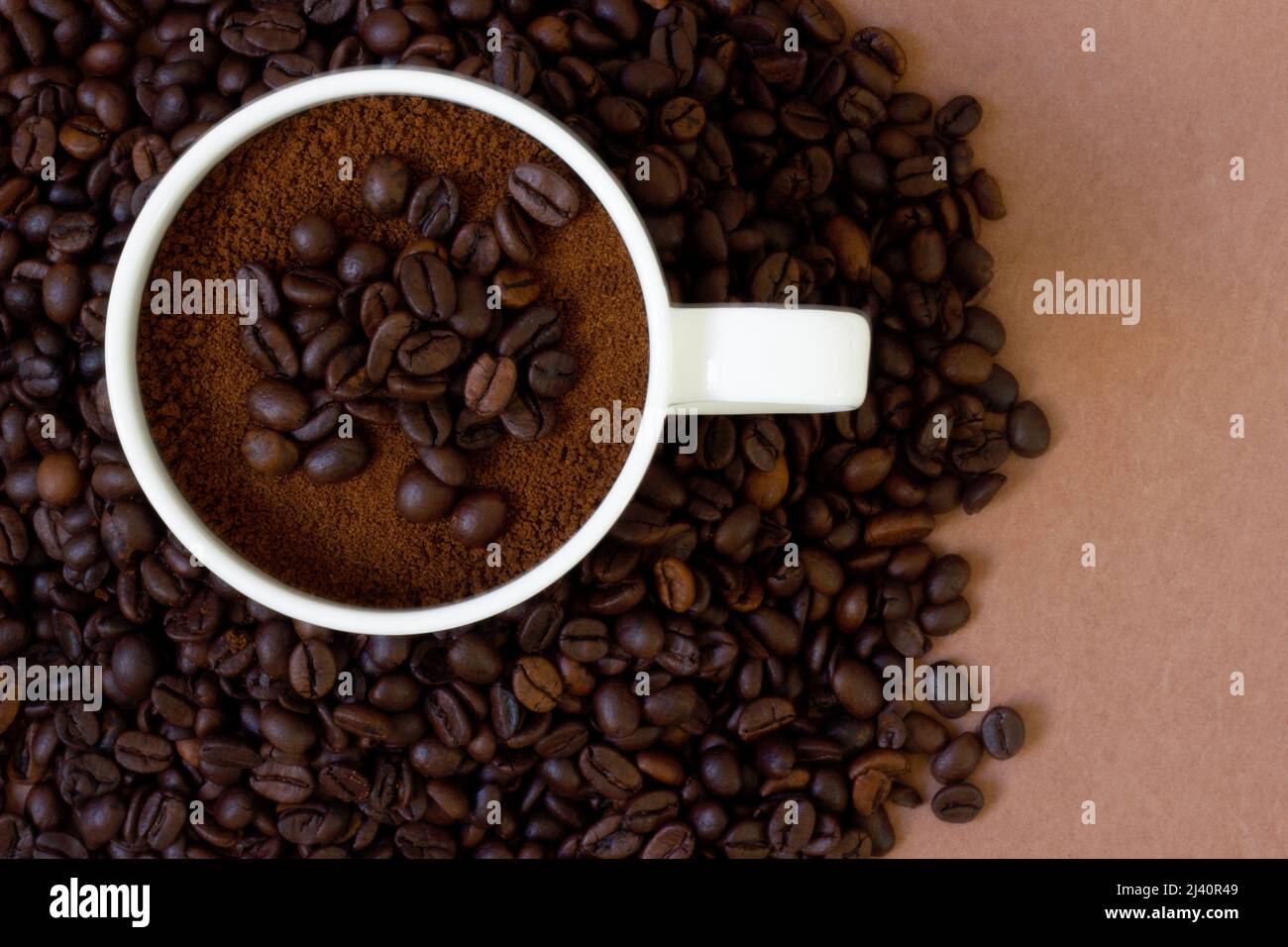 Freshly roasted coffee beans in the background and ground coffee in the cup on top. Background and texture available. Can be used for cafes Stock Photo