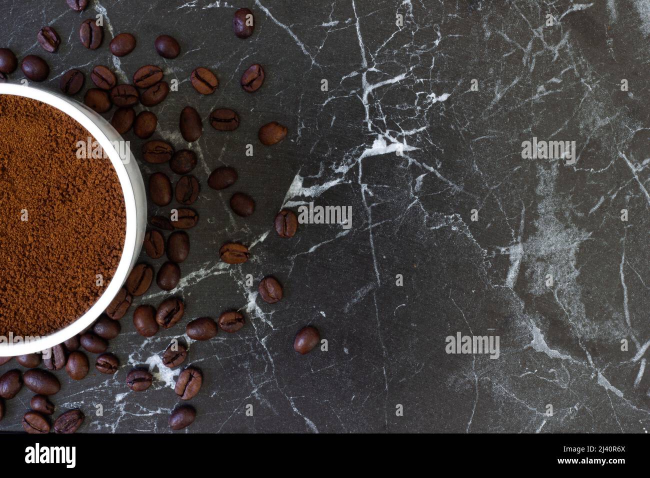 Freshly roasted coffee beans in the background and ground coffee in the cup on top. Background and texture available. Can be used for cafes Stock Photo