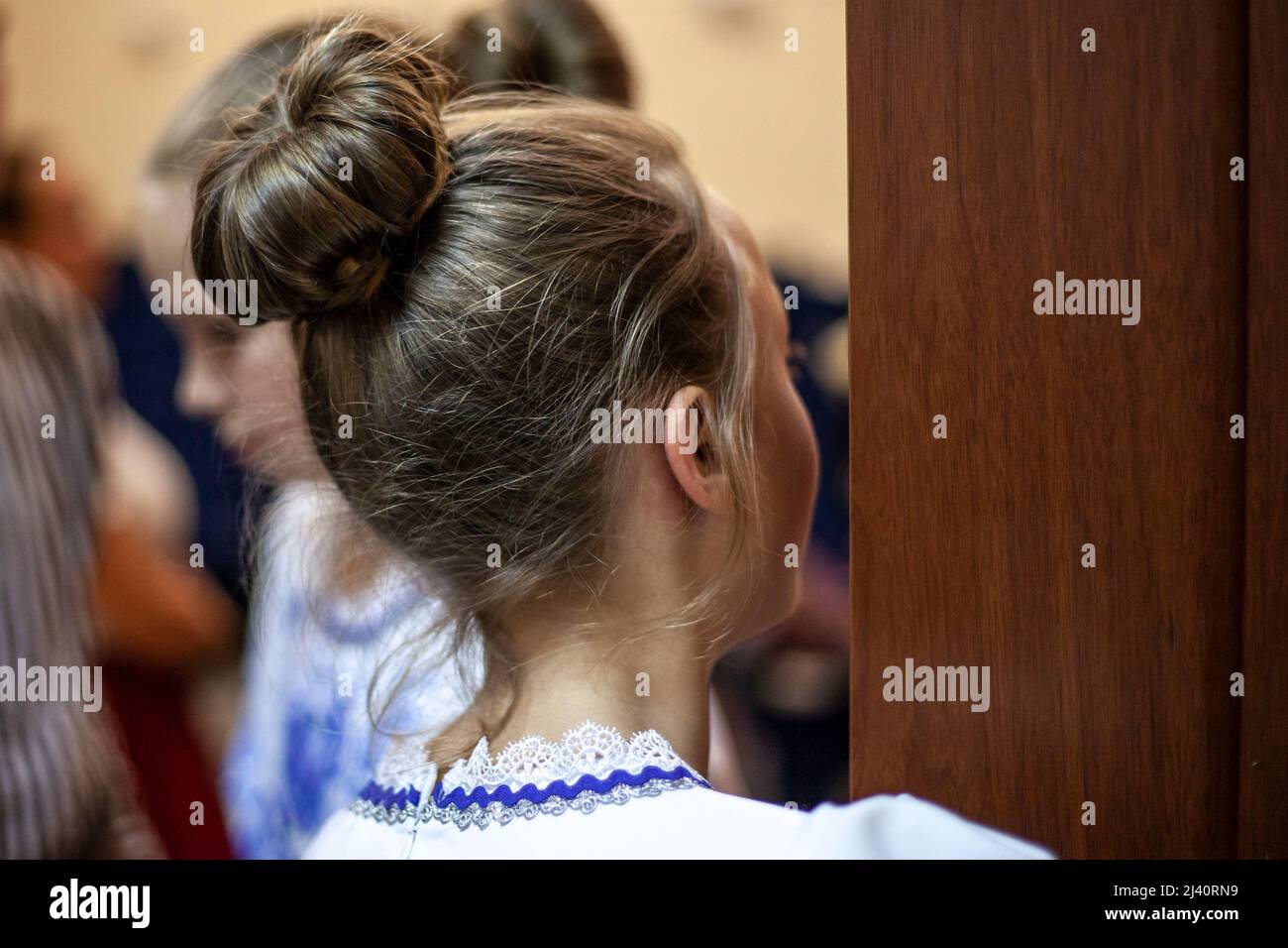 Hairstyle hair tied in a bun. The girl is looking out the door. A teenager with a classic haircut. Human head rear view. Stock Photo