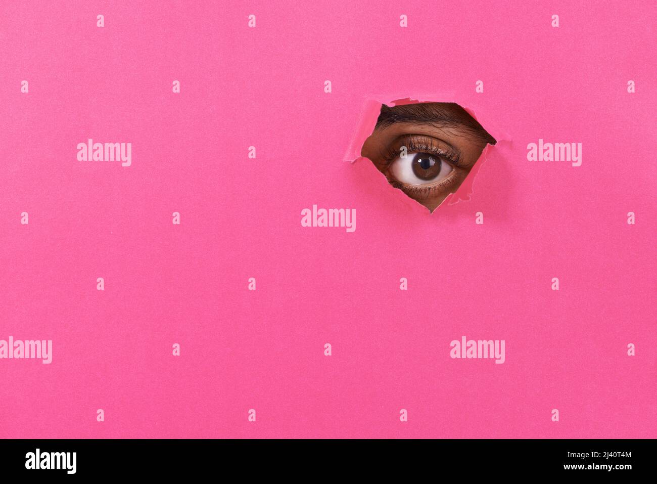 I see you. A view of a mans eye looking through a hole in some colorful paper. Stock Photo