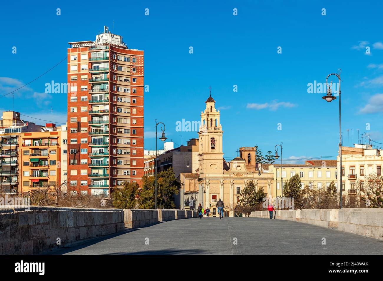People walking on pedestrian bridge as residential building and catholic church on background in Valencia, Spain. Stock Photo