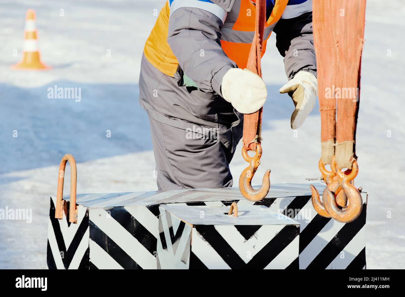 Slinger in work clothes hooks control load with hook. Authentic scene work at production base on street of winter day. Training and education of slingers. Stock Photo