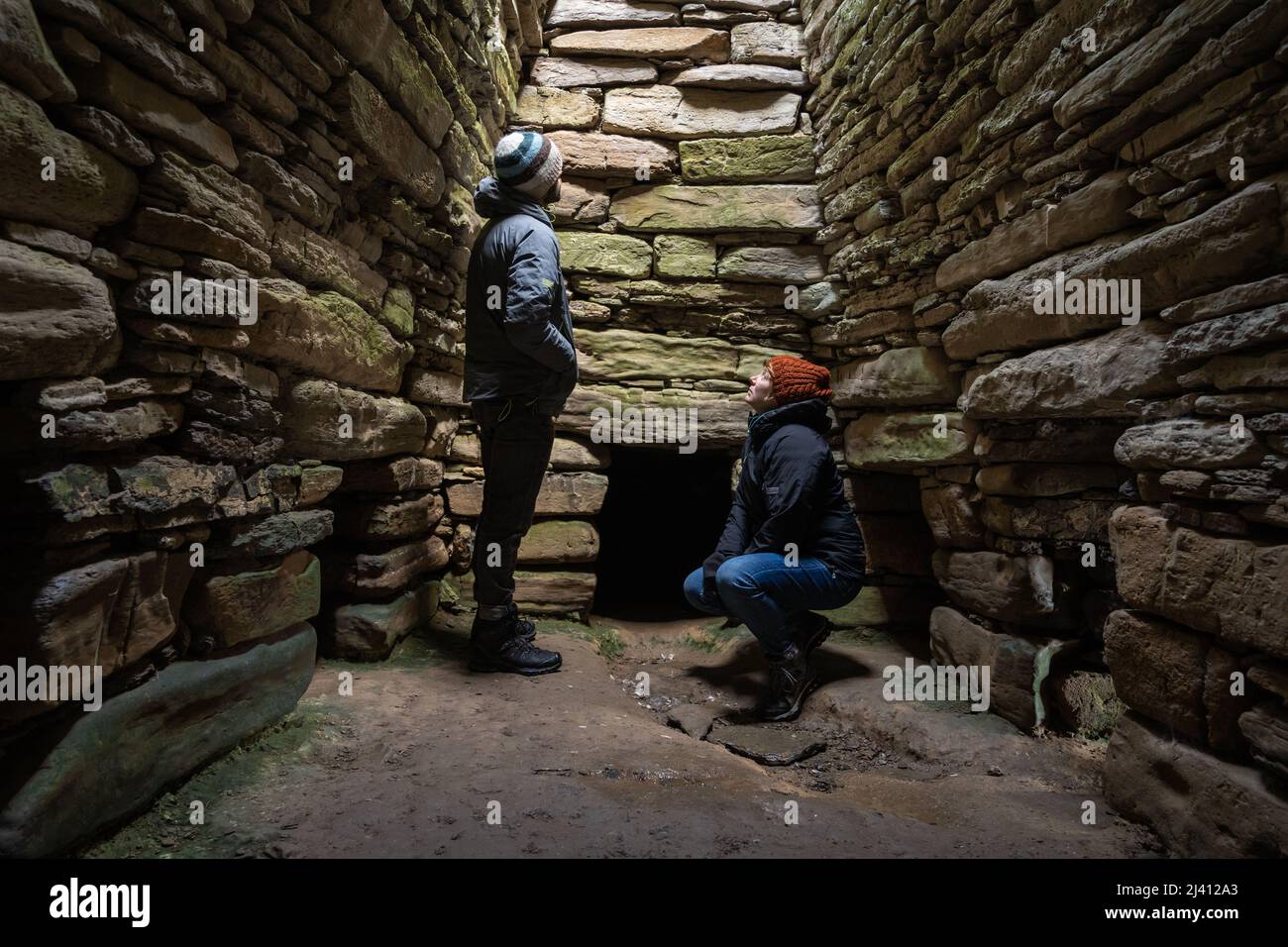 A male and a female tourist look up towards a skylight inside the Neolithic Quoyness Chambered Cairn on Sanday, Orkney. Stock Photo