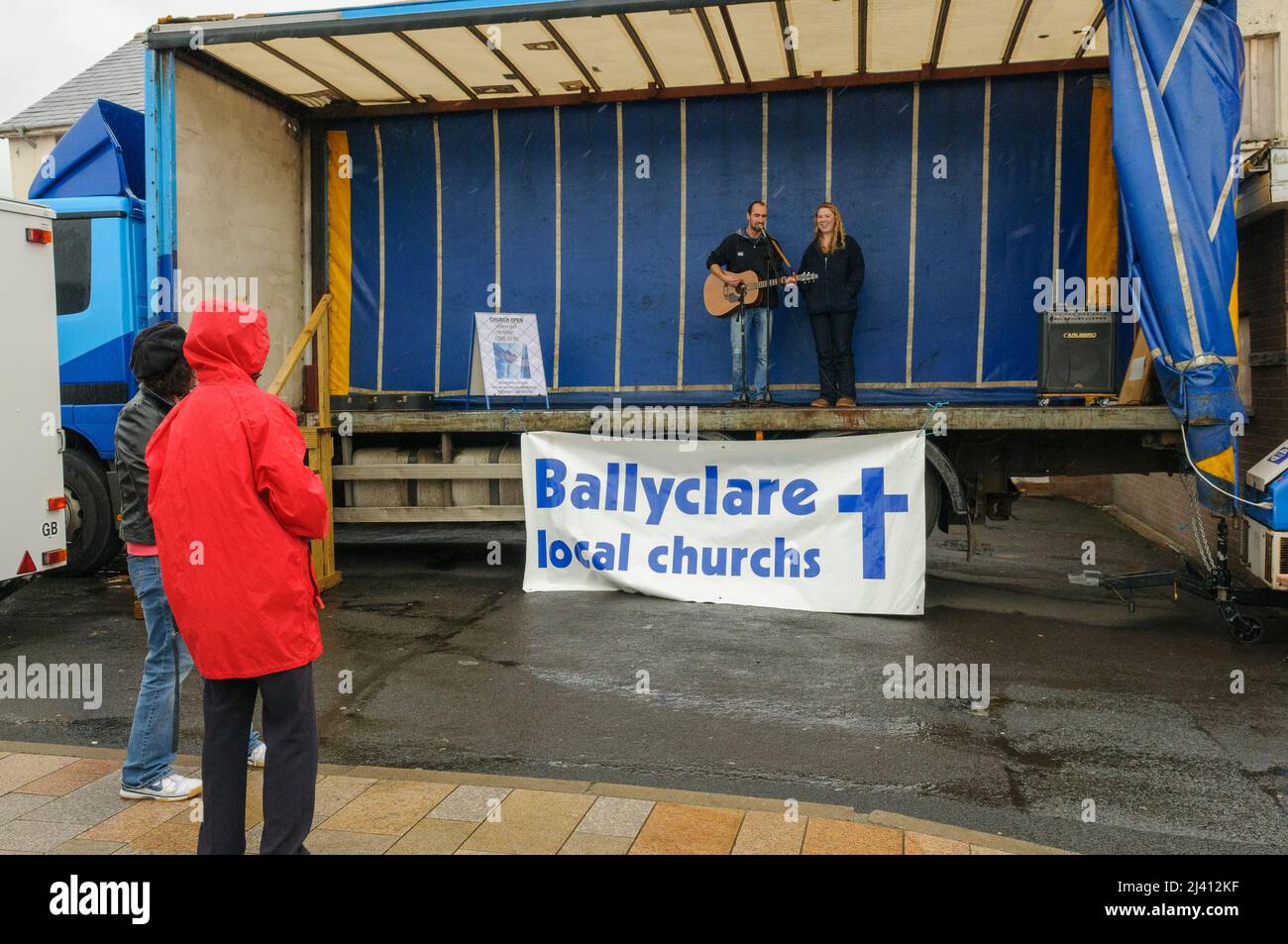 Ballyclare, Northern Ireland. 21st May 2011.  Two people watch a singer and guitarist perform on the back of a lorry with a mis-spelled sign saying 'Ballyclare local churchs [sic]' Stock Photo