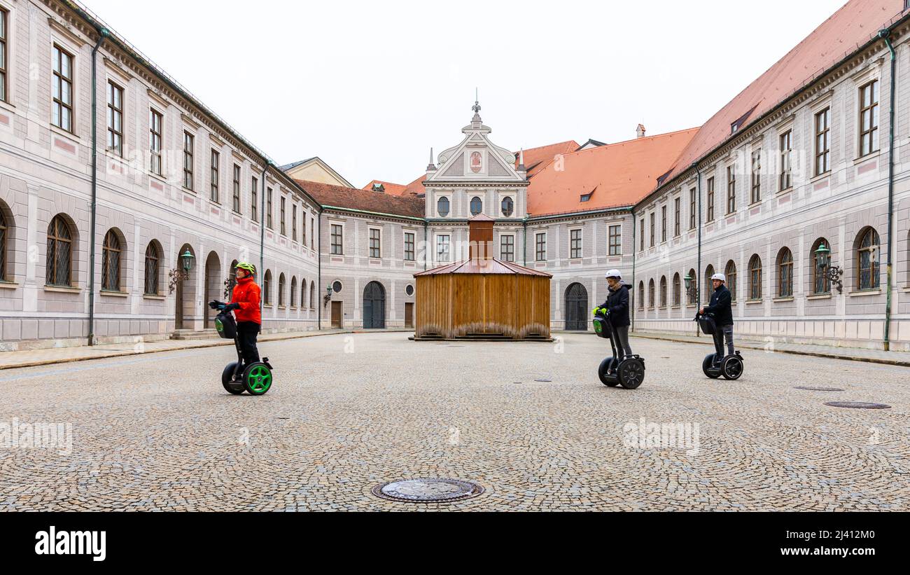 Munich, Germany - November 5, 2019: Three people drive two-wheeled electric vehicles on brick ground inside old public building for sightseeing tour. Stock Photo