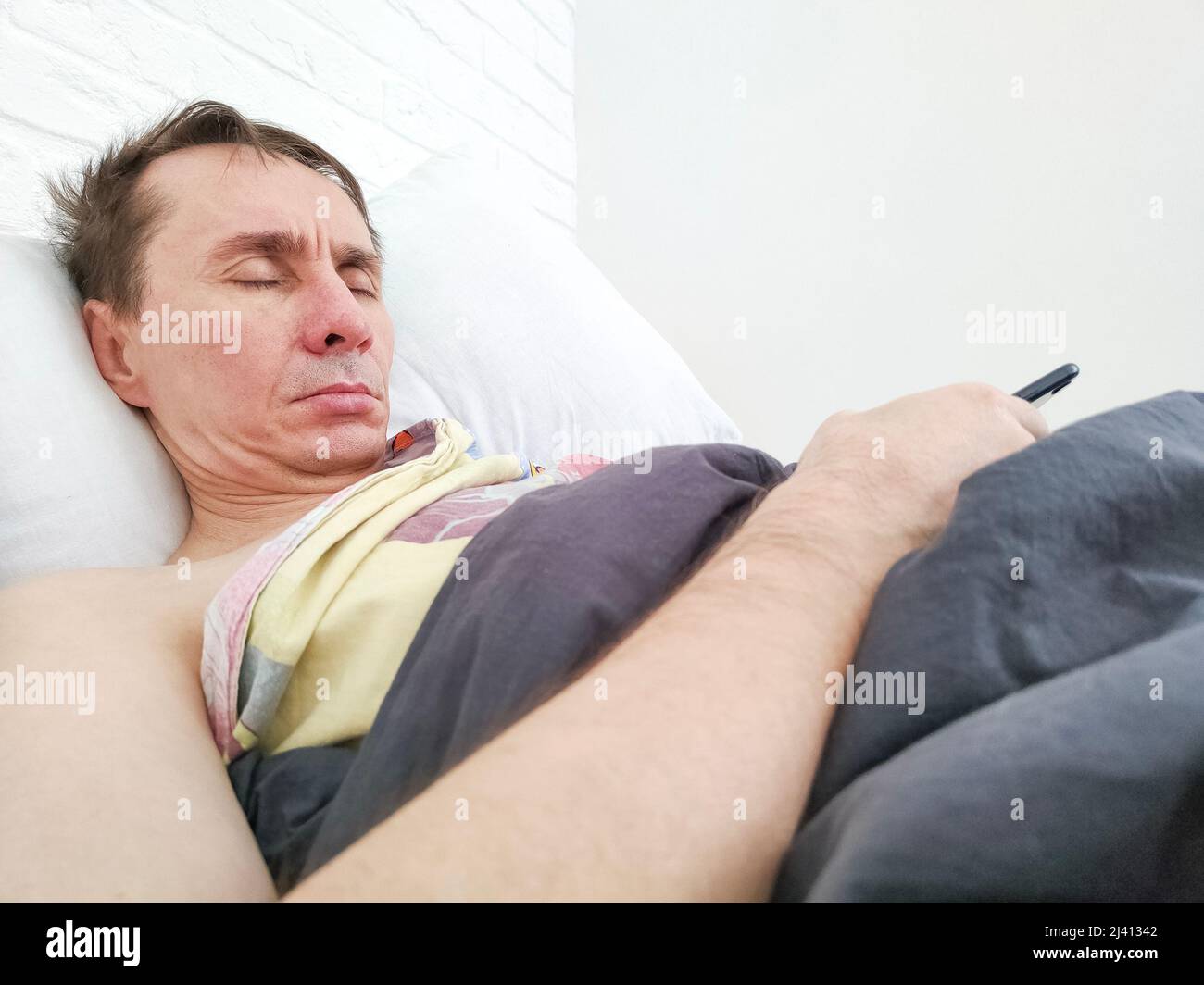 Man sleeping in bed under blanket with phone in his hands in the