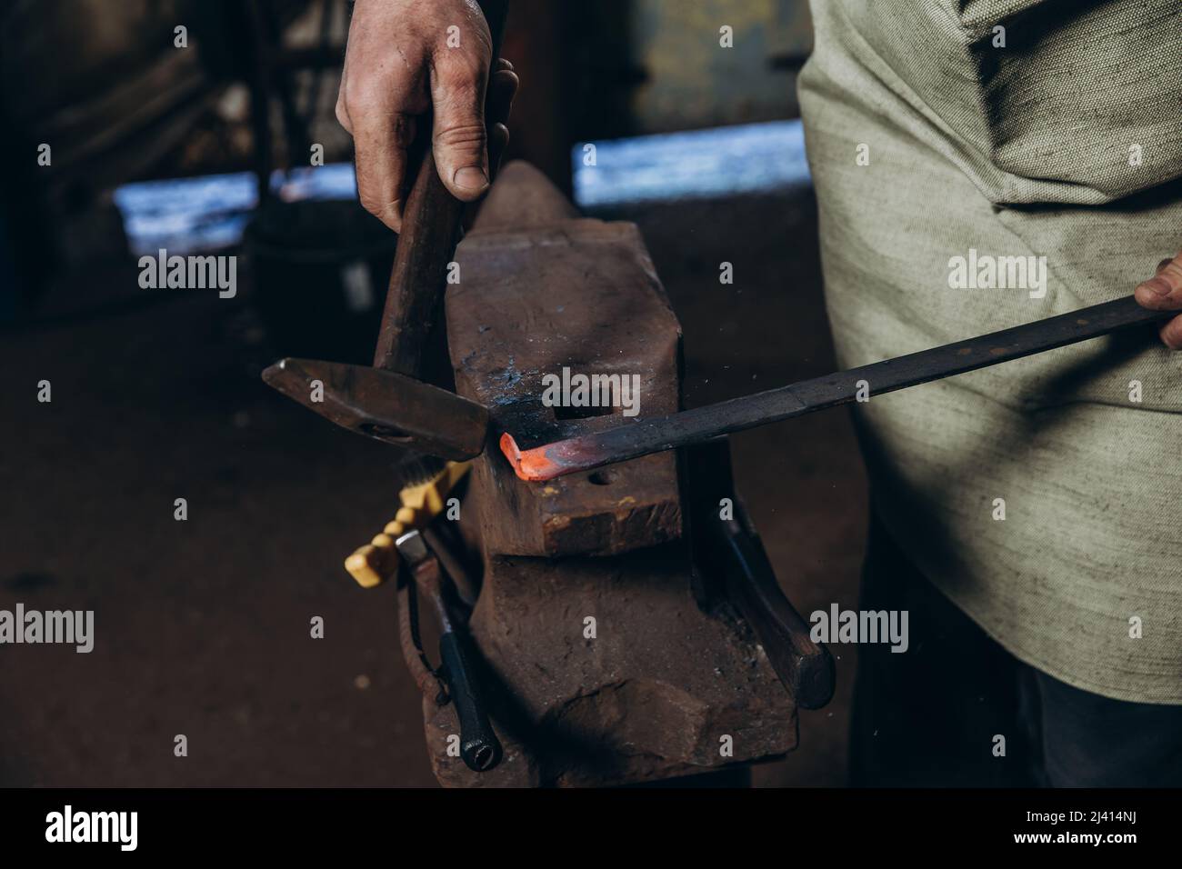 The blacksmith manually forging the red-hot metal on the anvil in smithy. Hard work. Energy and power. Concept of labor, retro professions Stock Photo