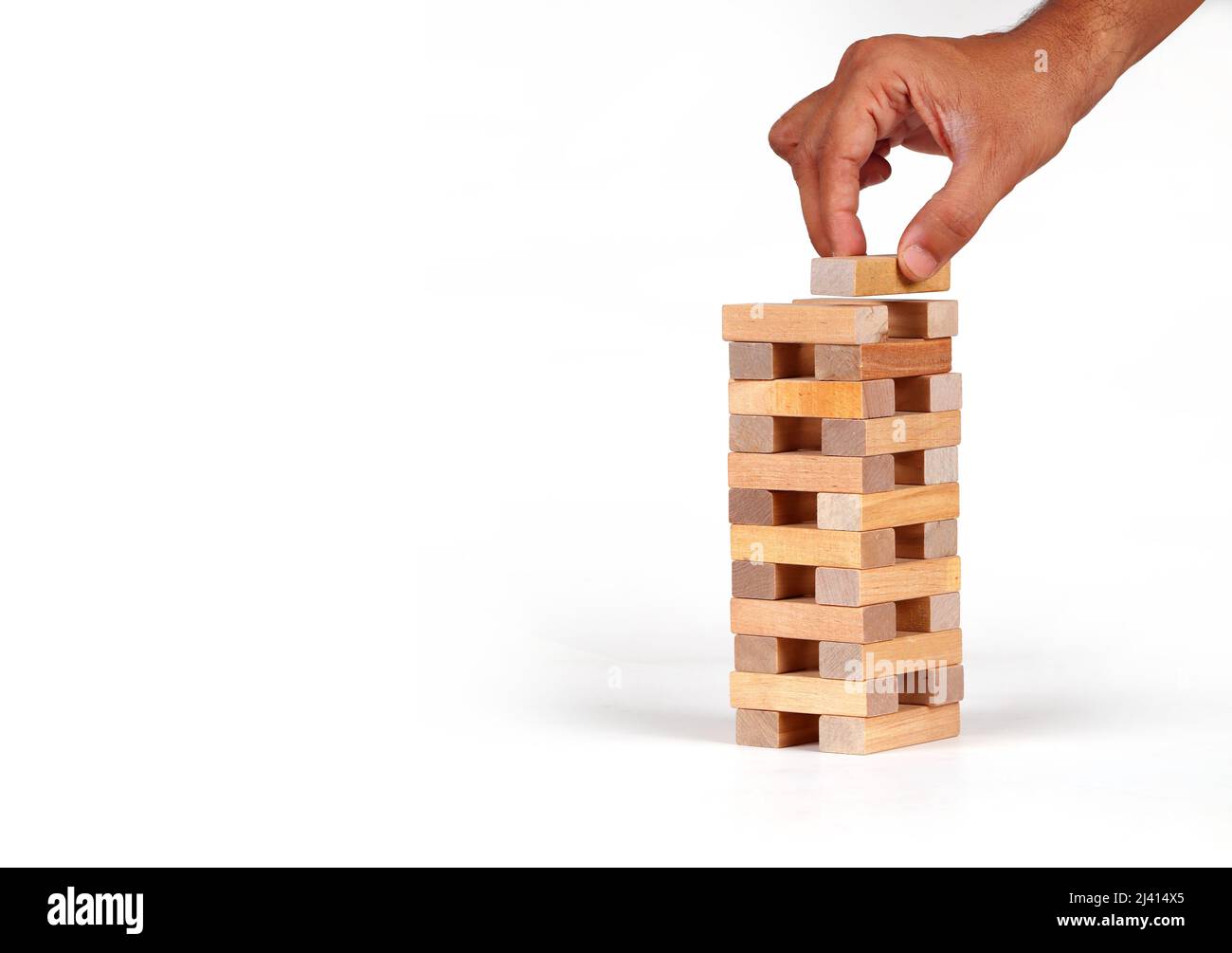 Man's hand put one block to the tower stack from wooden blocks toy with isolated background. Stock Photo