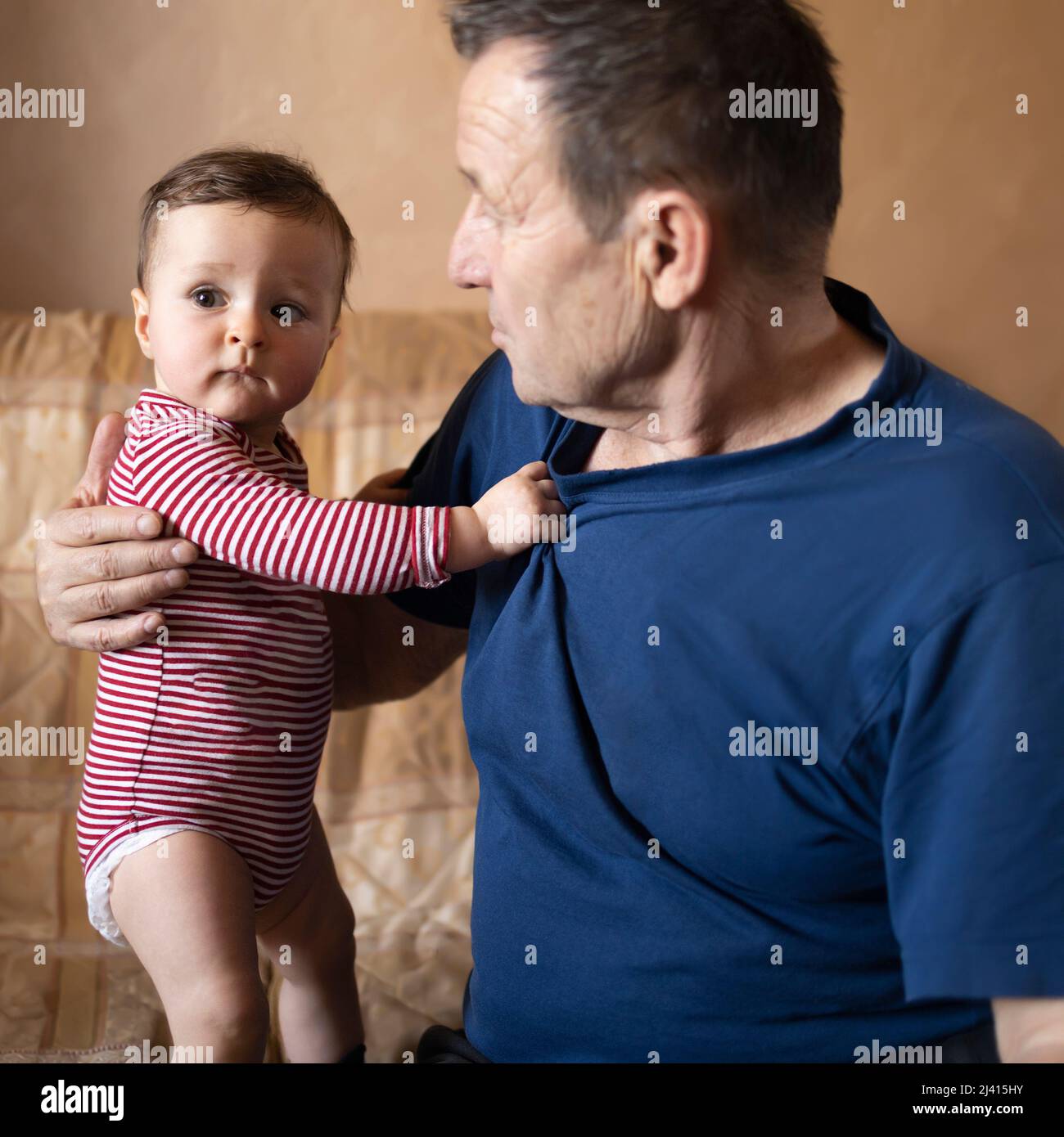 Small baby holding on to her grandpa and learning how to stand Stock Photo