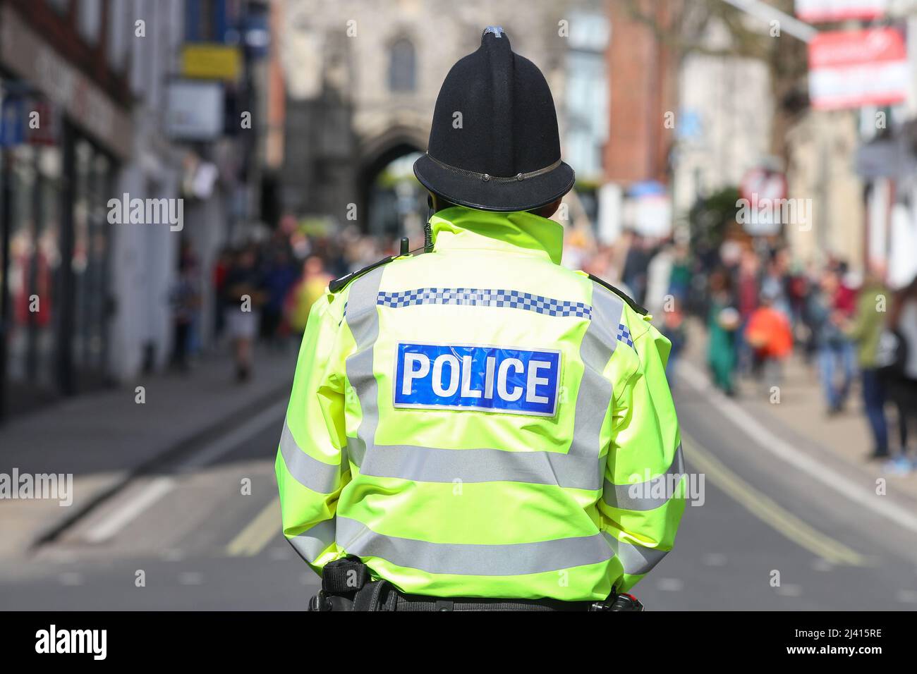 A Hampshire Police officer wearing a hi vis jacket and a traditional police helmet pictured from behind in Winchester in the UK. Stock Photo