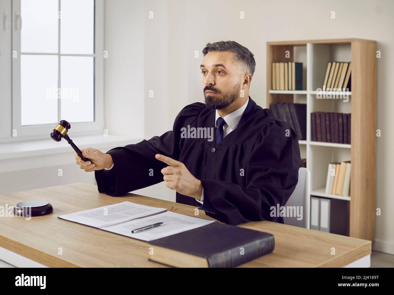Judge in gown hitting sound block with gavel and giving judgment at the end of trial Stock Photo