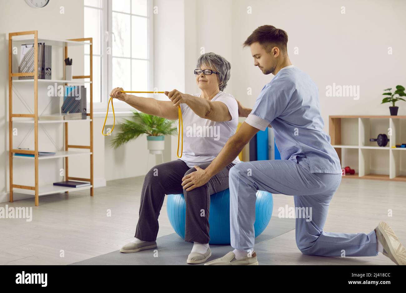 Doctor helping senior patient with osteoporosis do physiotherapy exercises on fit ball Stock Photo