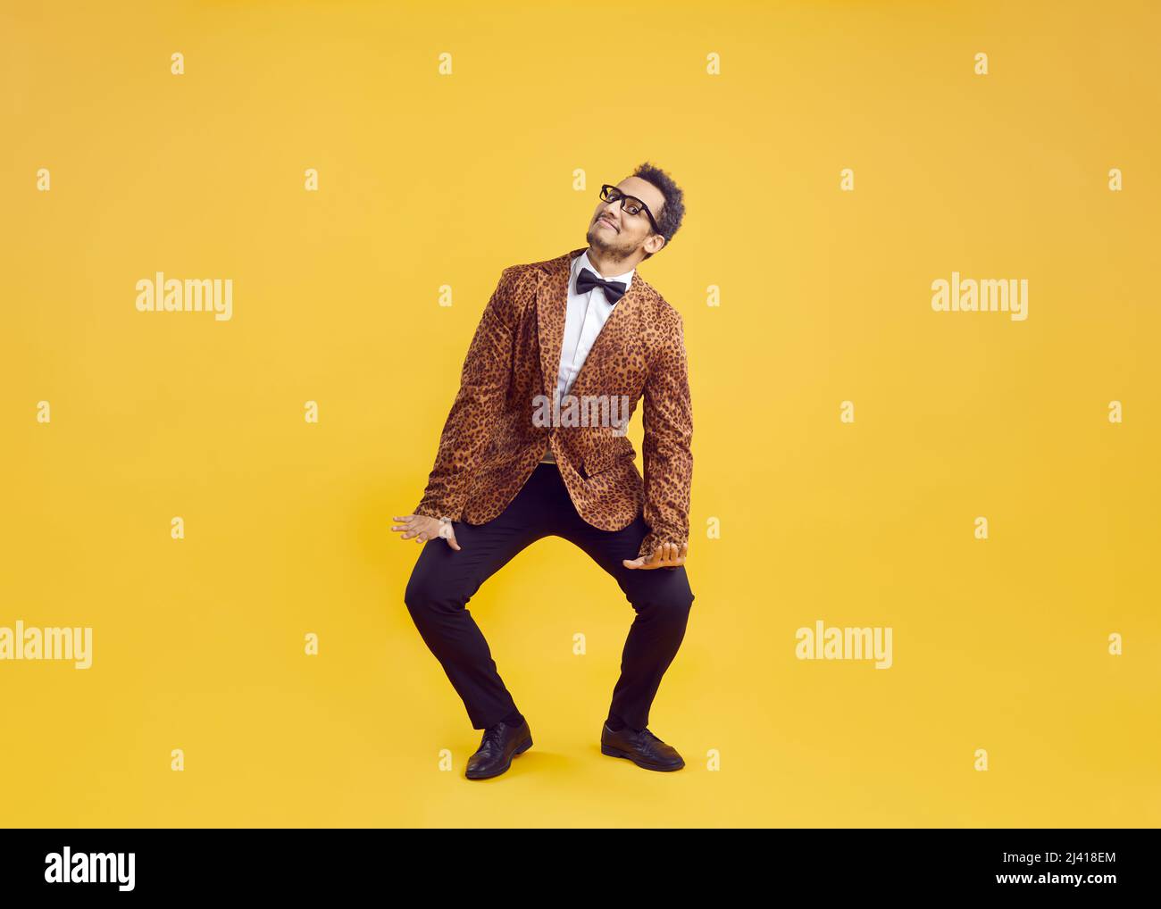 Happy funny goofy black man in leopard jacket dancing on yellow studio background Stock Photo