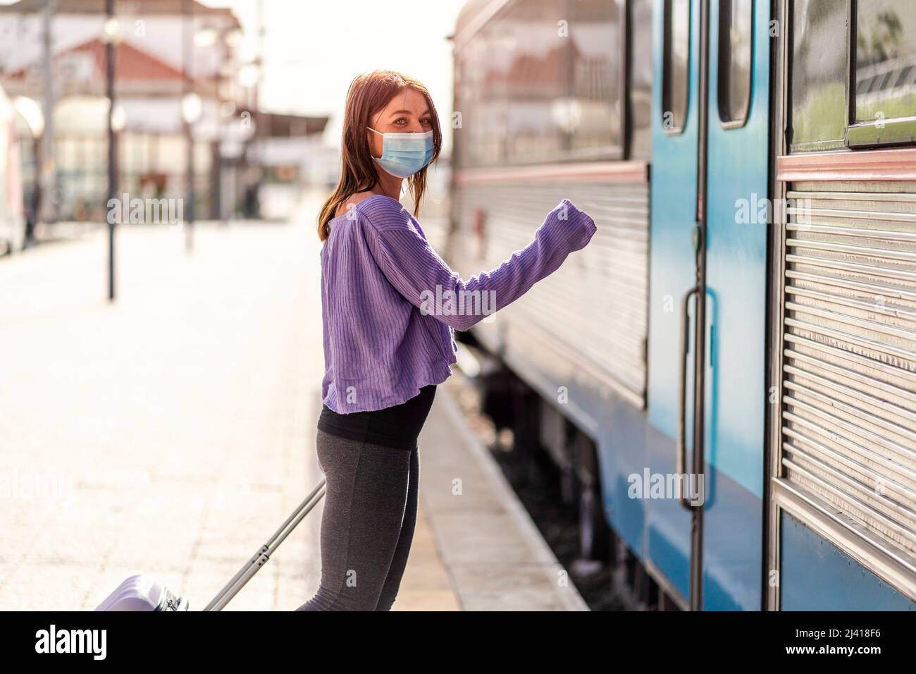 A young woman wearing mask and with a luggage ready to enter the train and depart Stock Photo