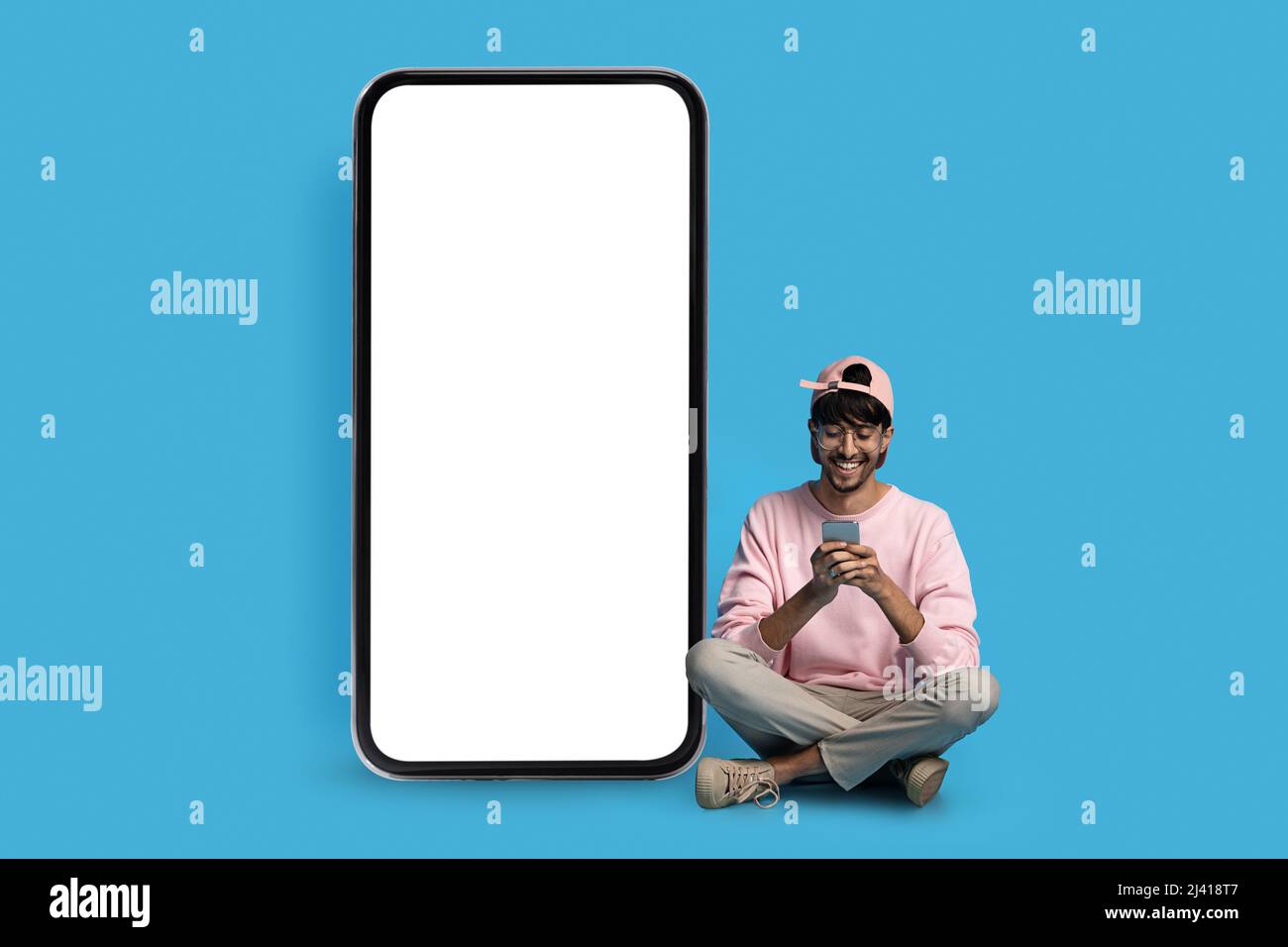 Cheerful hindu guy hipster sitting by huge smartphone Stock Photo