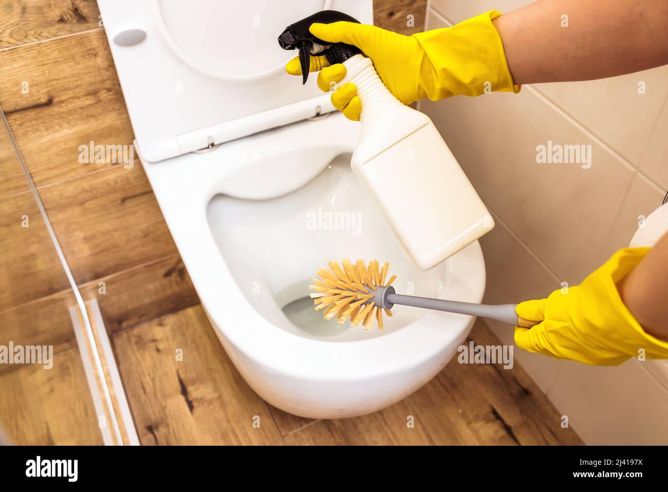 Closeup of hands using brush and cleaning solution to disinfect toilet