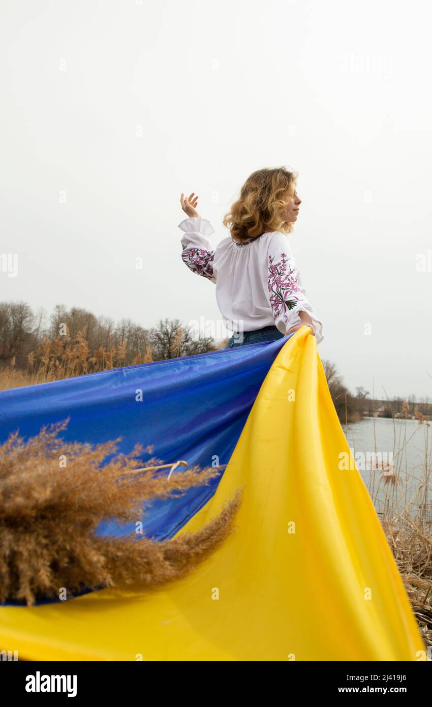 young woman in an embroidered blouse stands with a fluttering blue and yellow Ukrainian flag. the pride of the nation, I am Ukrainian. People are agai Stock Photo