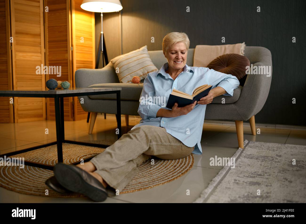 Old woman reading book sitting on sofa Stock Photo