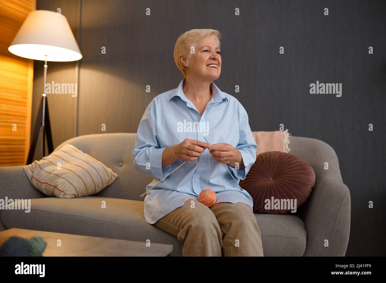 Smiling grandmother knitting sitting at home sofa Stock Photo