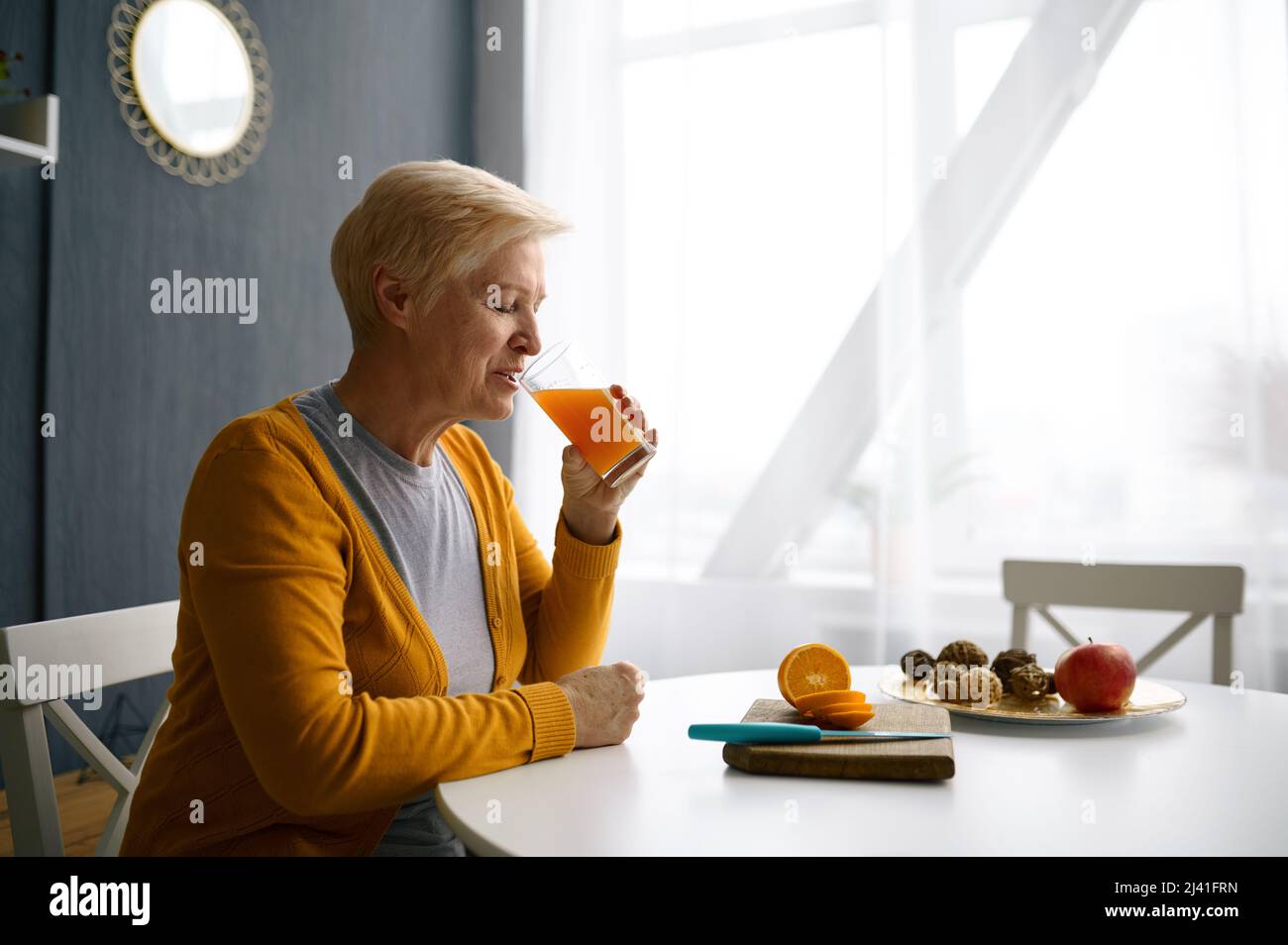 Smiling grey-haired woman holding glass with juice Stock Photo