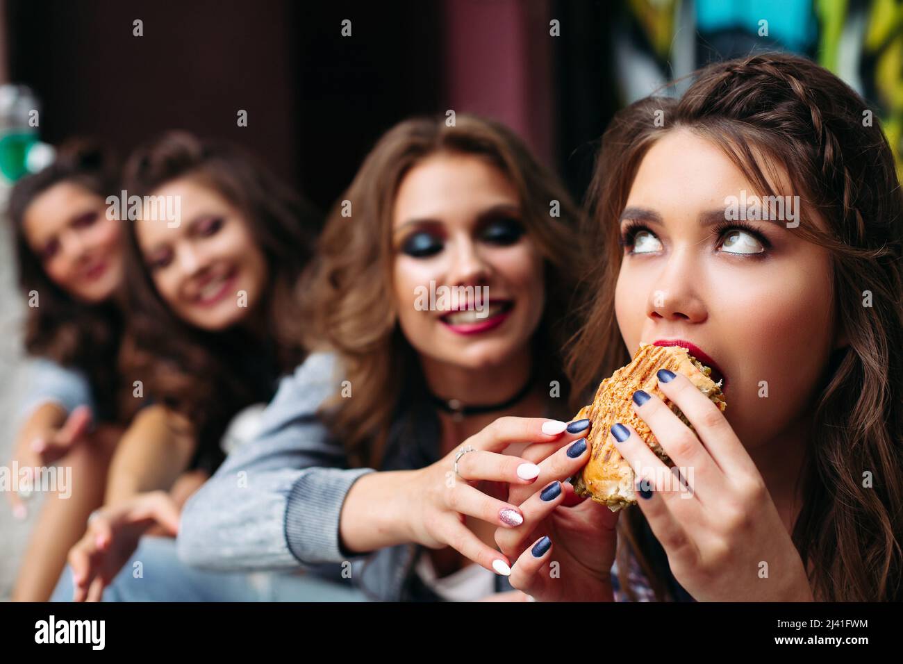 Smiling friends want to take girlfriend's burger while she eating it. Stock Photo