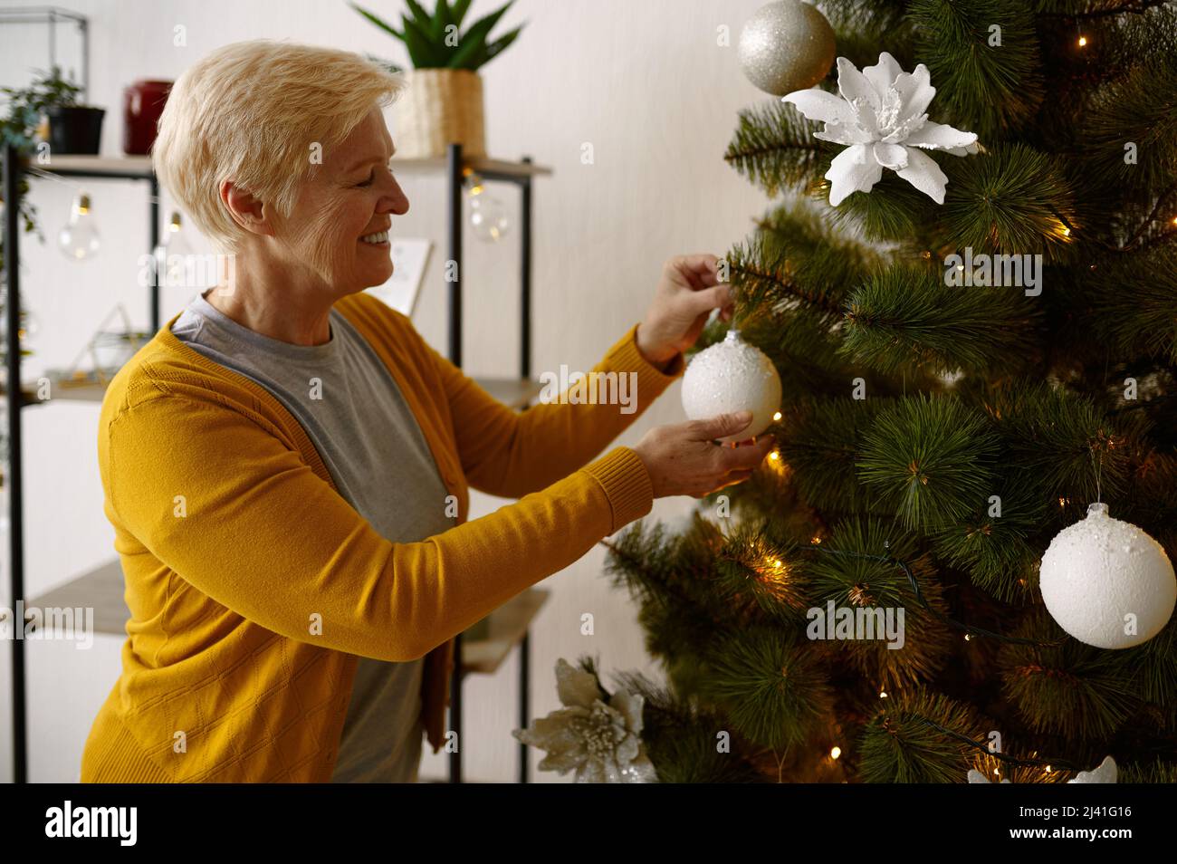 Old woman hanging Christmas tree ball decoration Stock Photo