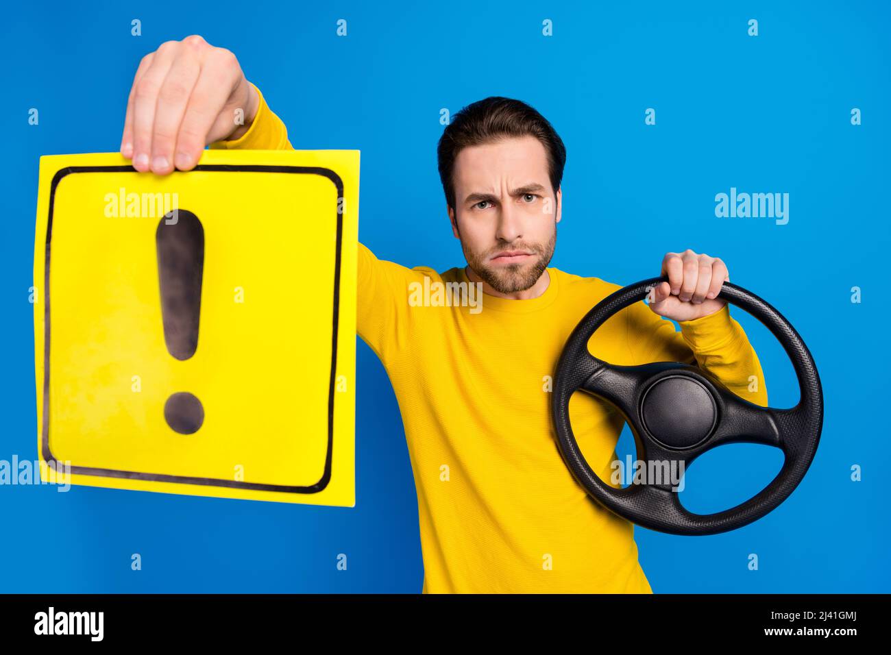 Portrait of attractive serious guy holding steering wheel exclamation