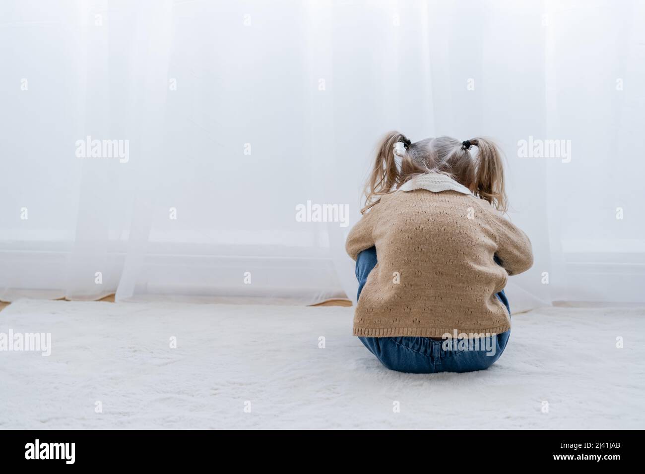back view of upset child sitting on floor near white curtain Stock ...