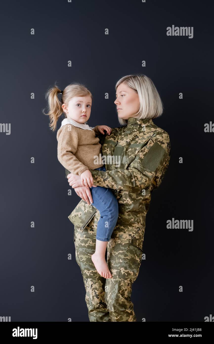 serious woman in camouflage holding little daughter in hands isolated