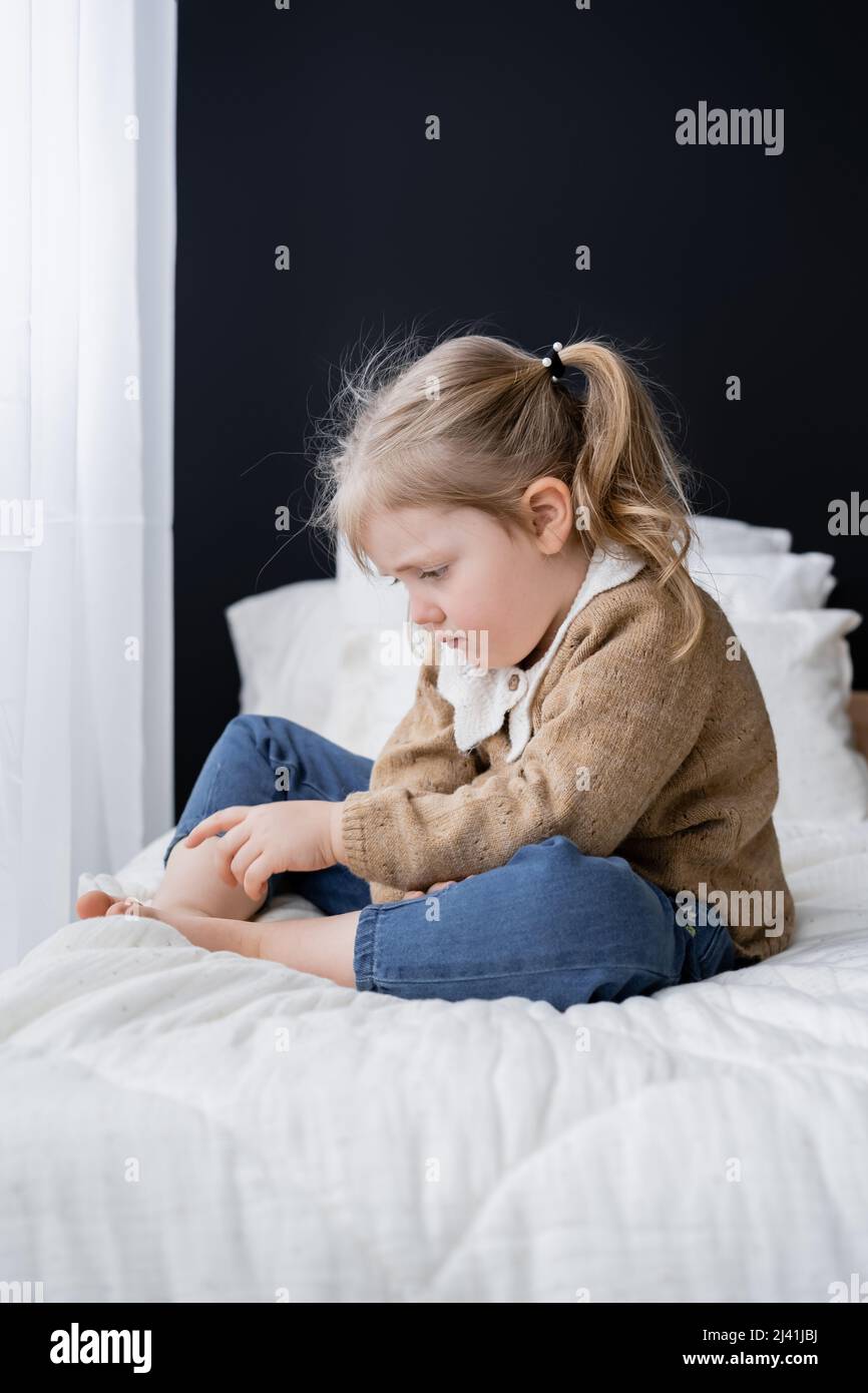 upset barefoot child sitting on bed at home Stock Photo