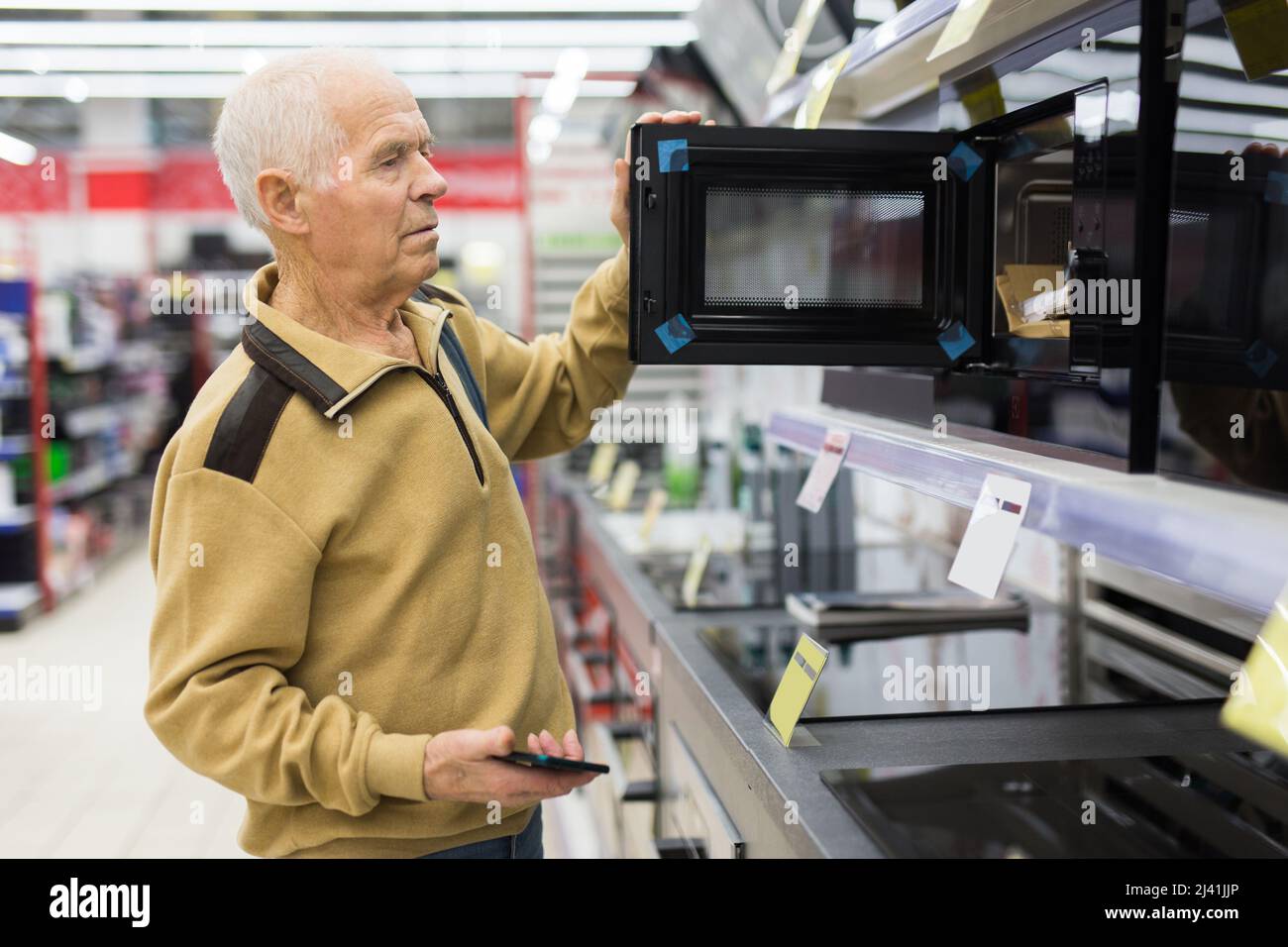 elderly man choosing microwave oven in showroom of electrical appliance