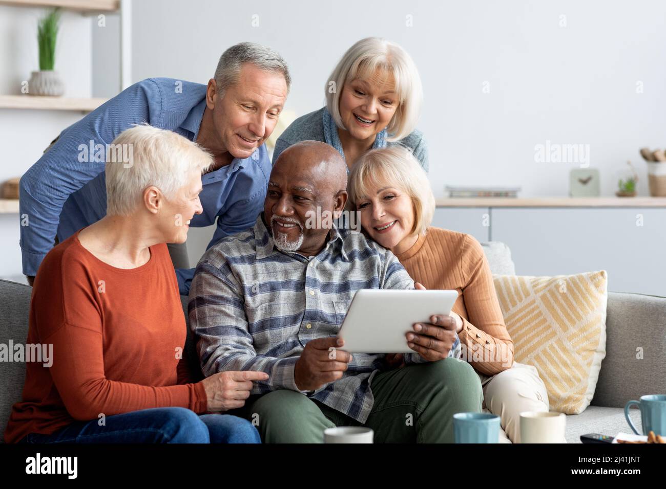 Cheerful elderly people spending time together at home, using gadgets Stock Photo