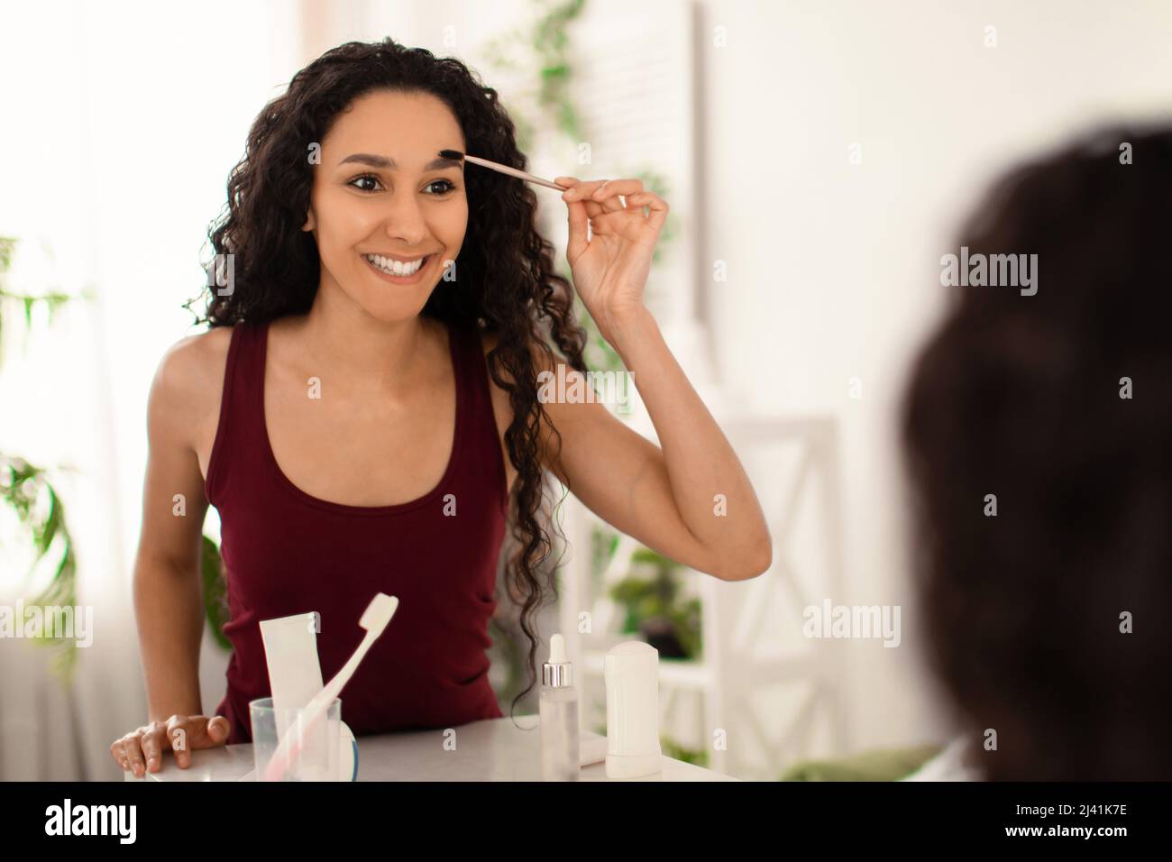 Charming millennial woman applying eyebrow mascara near mirror at home, empty space Stock Photo