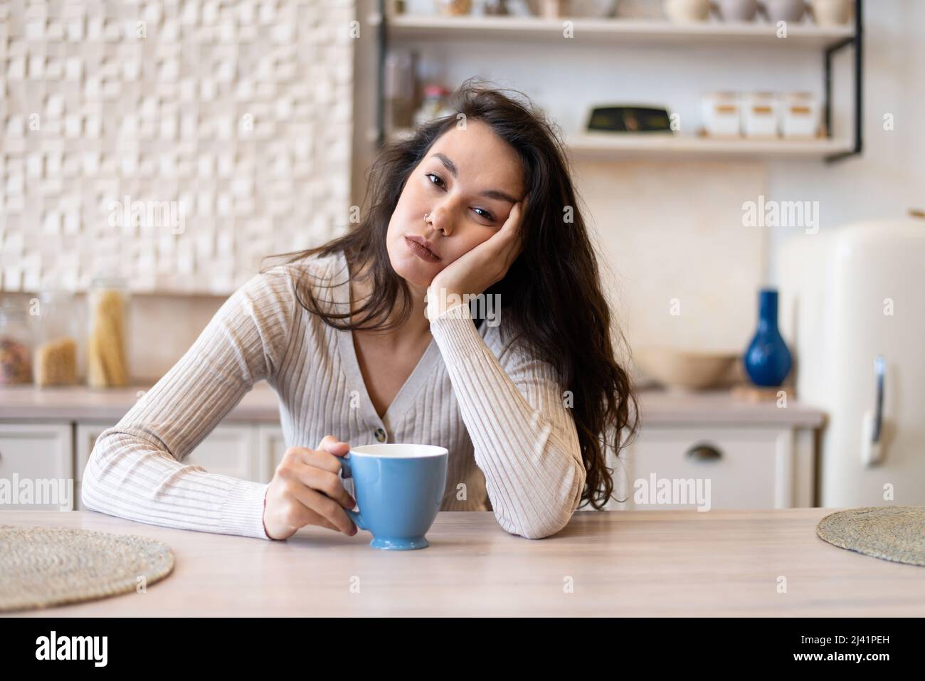 Tired and sleepy woman drinking coffee in the morning, feeling exhausted, suffering from insomnia, sitting in kitchen Stock Photo
