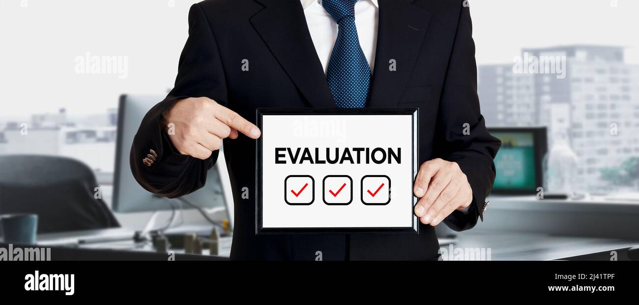 Businessman holds a signboard and points his finger to the word evaluation. Business performance evaluation concept. Stock Photo