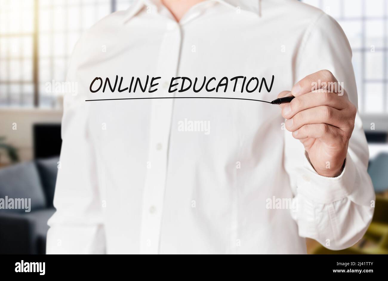 Businessman hand holds a pen and underlines the words online education on a virtual screen. Online distance training concept. Stock Photo