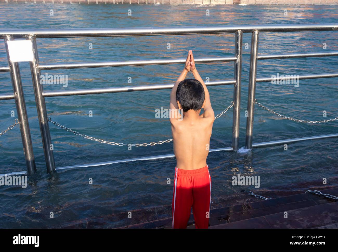young kid doing religious pryer of river at morning from flat angle image is taken at haridwar uttrakhand india. Stock Photo