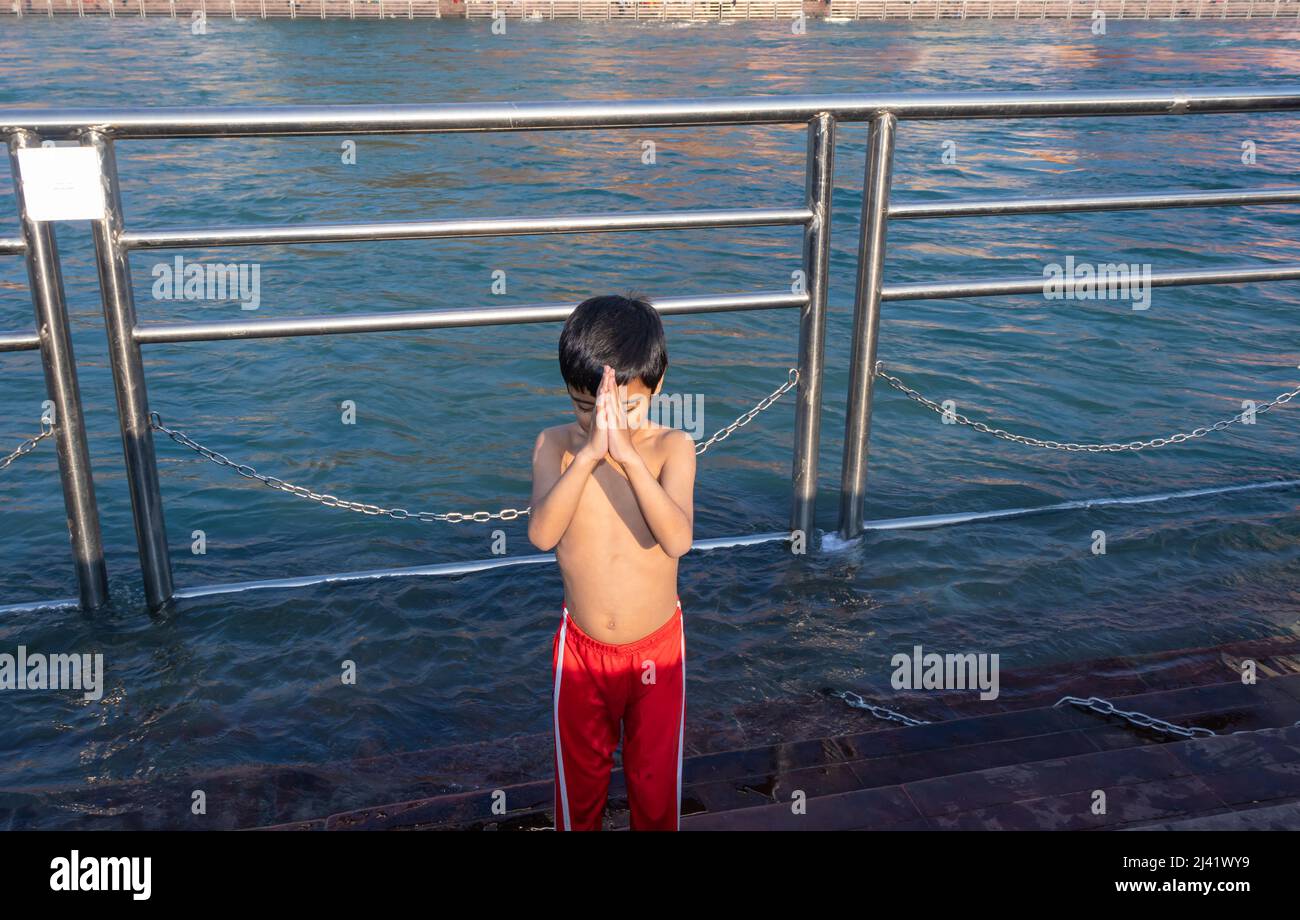 young kid doing religious pryer of river at morning from flat angle image is taken at haridwar uttrakhand india. Stock Photo