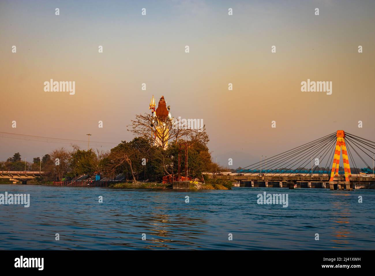 hindu god shiva statue and isolated cable bridge over ganges river from back with bright blue sky image is taken at haridwar uttrakhand india. Stock Photo