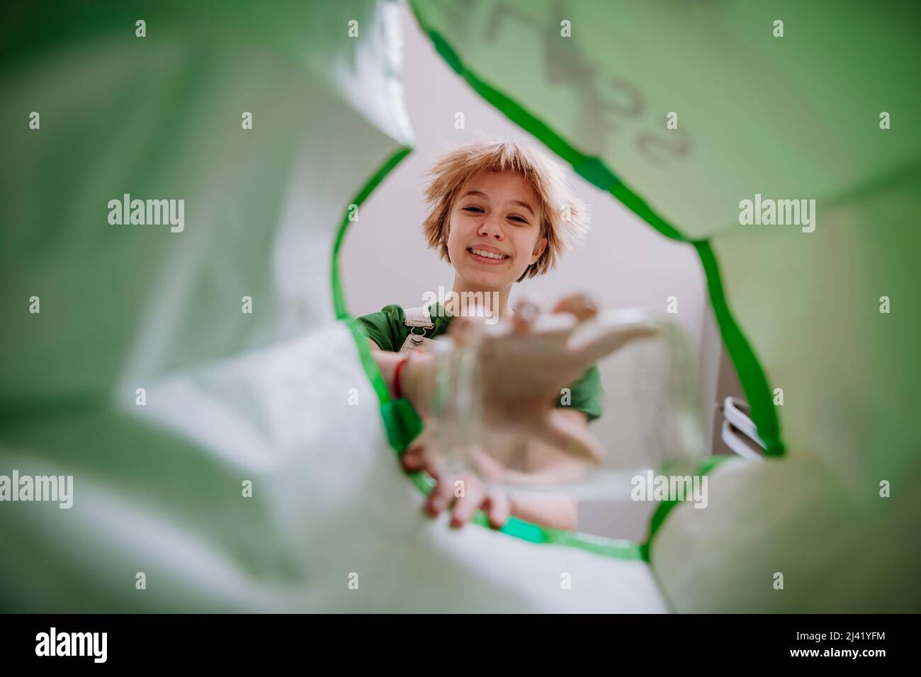 Image from inside green recycling bag of girl throwing a glass bottle to recycle. Stock Photo