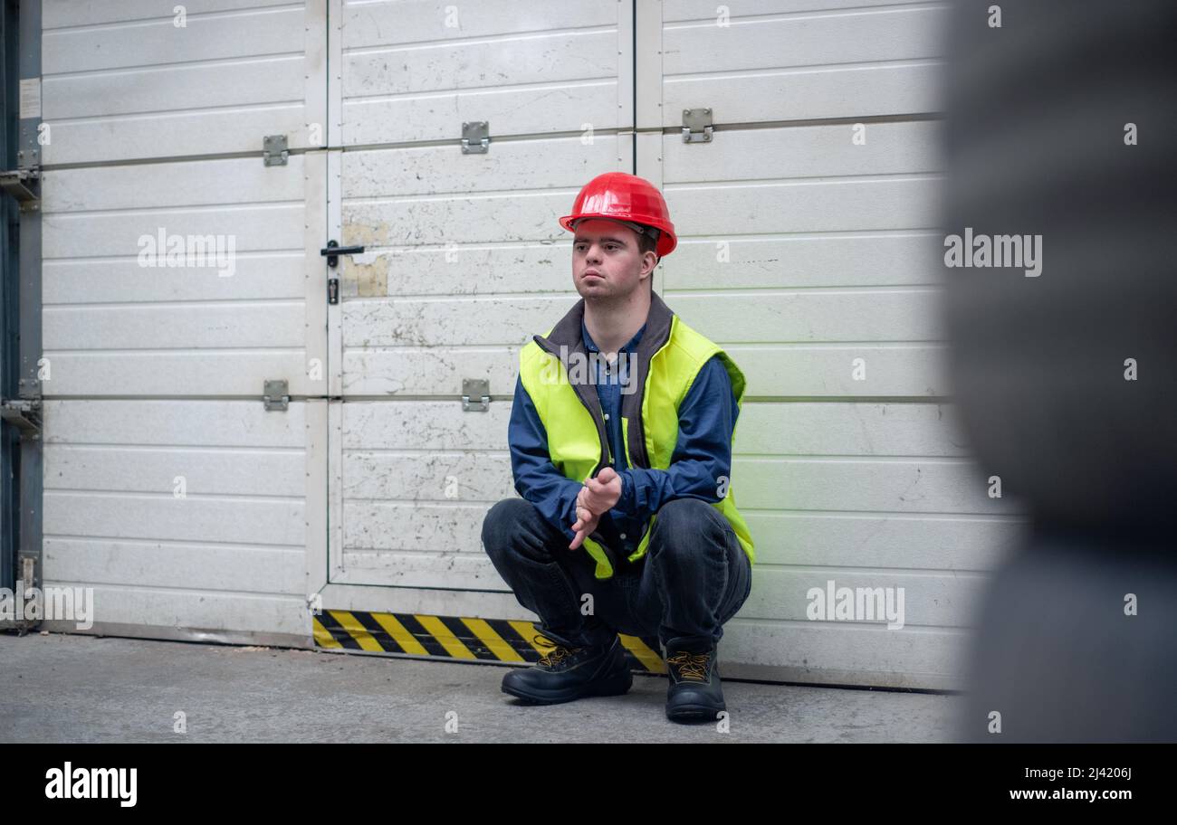 Young man with Down syndrome resting when working in insutrial factory, social integration concept. Stock Photo