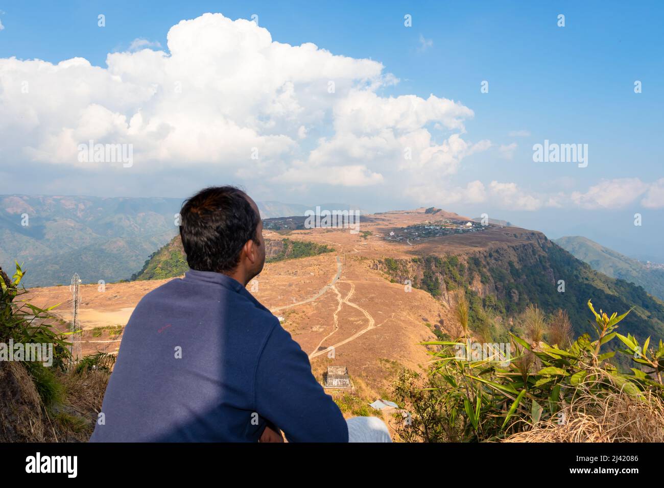 young man watching mountain top flat bed with flat sky at morning from flat angle image taken at nongnah meghalaya india. Stock Photo