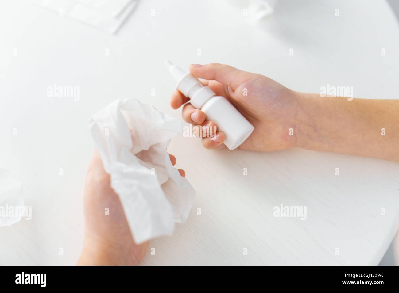 Child hands hold bottle nose spray and paper tissue on white background. Runny nose treatment Stock Photo