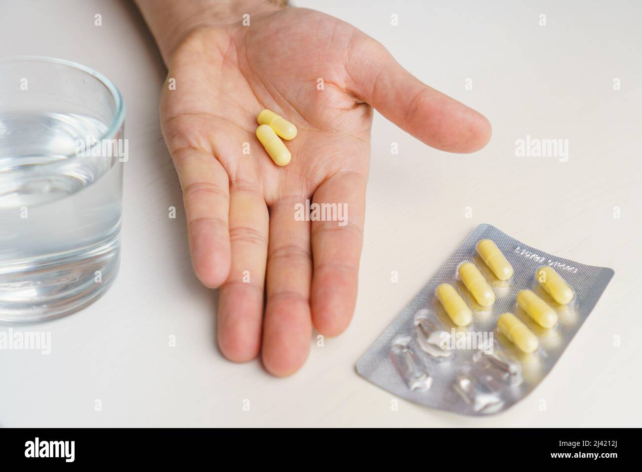 Close-up hand holding medicine capsule and glass of water at background. Taking pill concept Stock Photo