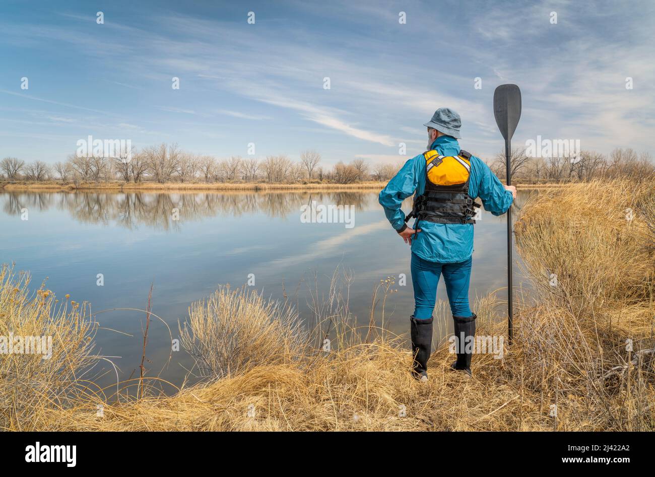 senior male stand up paddler wearing life jacket on a shore of calm lake in early spring scenery in Colorado Stock Photo